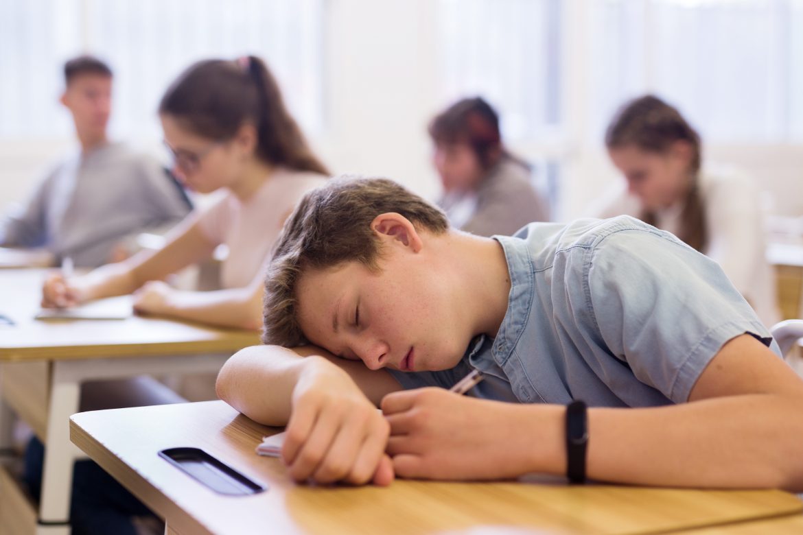 Tired bored teenage school boy sleeping at desk in classroom