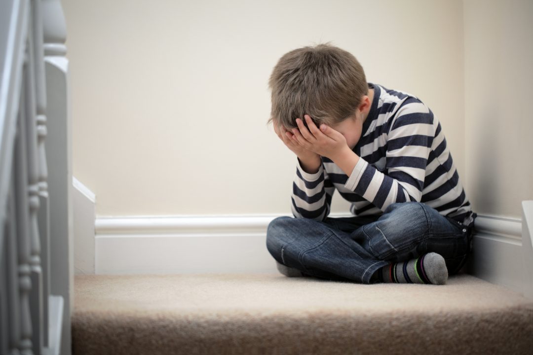 Upset problem child with head in hands sitting on staircase concept for bullying, depression stress or frustration